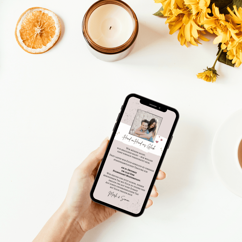 Hand in Hand ins Glück: Digitale Einladungskarte in zarten beige- und creme-Tönen. Ein Foto des Brautpaares steht im Mittelpunkt der Einladungskarte, daneben dezente Herzen und leichte Sandspuren